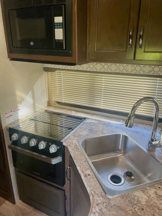 Inside a modern rv rental: a compact kitchen with microwave, Furrion stove, and sink, bathed in sunlight.. Thor Freedom Elite 2019