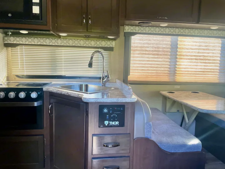 Explore this RV rental's compact kitchen with a sink, stove, microwave, and dinette area perfect for your next trip.. Thor Freedom Elite 2019