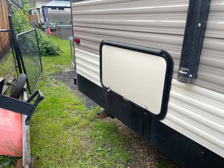 Side of an RV rental with an open exterior storage compartment, showing its striped siding and black awning post.. KZ Sportsmen SE 260BHSE 2020