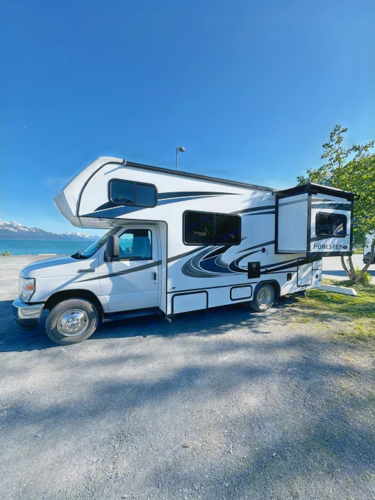White Forester RV rental by a scenic bay with snow-capped mountains. Ideal for outdoor adventures & travel, under a clear blue sky.. Forester LE 2022