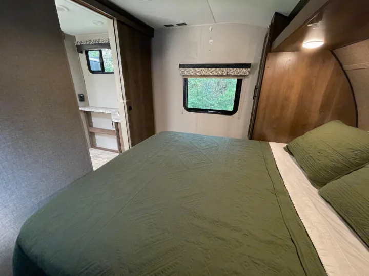 Cozy RV rental bedroom with green bedding, a bright window, and a hallway leading to other areas.. Connect 261RL 2018