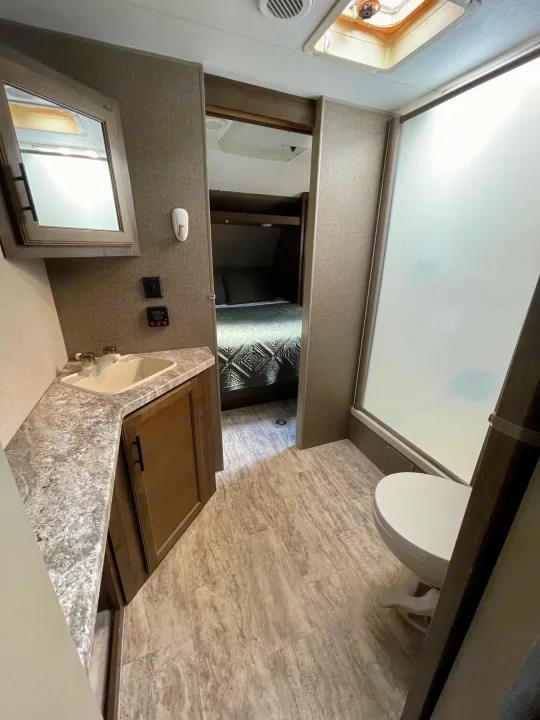 RV rental bathroom featuring a sink, mirror, toilet, shower, and a glimpse into the connected bedroom.. Connect 261RL 2018