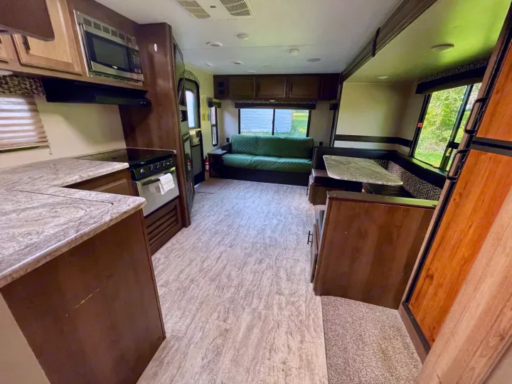 Inside a well-appointed RV rental, featuring a full kitchen, comfortable dinette, and cozy living area with a green sofa.. Connect 261RL 2018