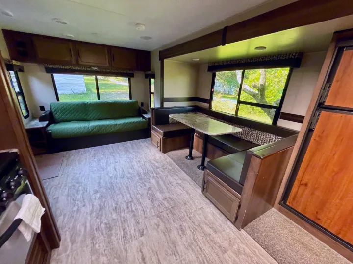 Cozy RV rental living area featuring a green sofa, dinette booth, and ample natural light from large windows.. Connect 261RL 2018