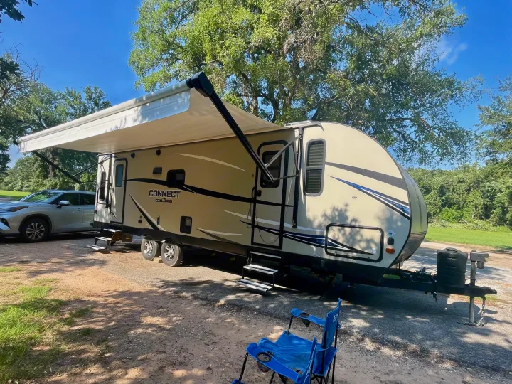 This RV rental travel trailer is set up with its awning out at a sunny campsite, ready for an outdoor adventure.. Connect 261RL 2018