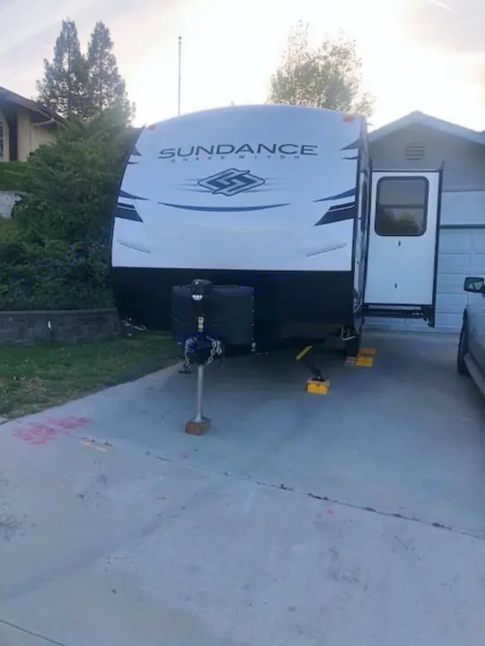 White Sundance travel trailer parked on a driveway with its door open, ready for an RV rental adventure.. Heartland RVs Other 2022