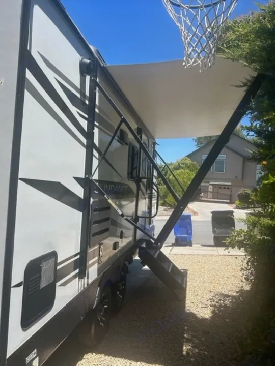 Experience comfort with this RV rental! Awning extended, steps down, parked on gravel, with a basketball hoop overhead.. Heartland RVs Other 2022