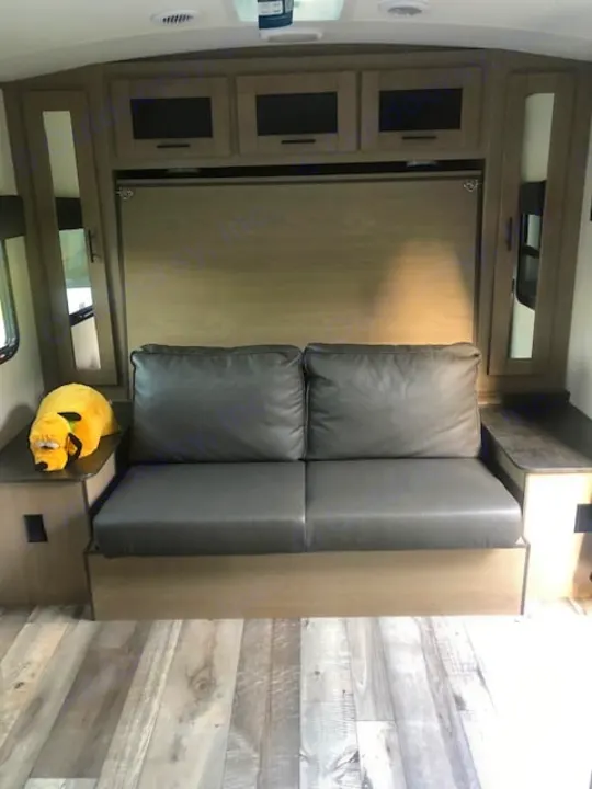 RV rental: Gray sofa, wall bed, cabinets, and wood floor. A yellow stuffed animal sits on the left side table.. Heartland RVs Other 2022