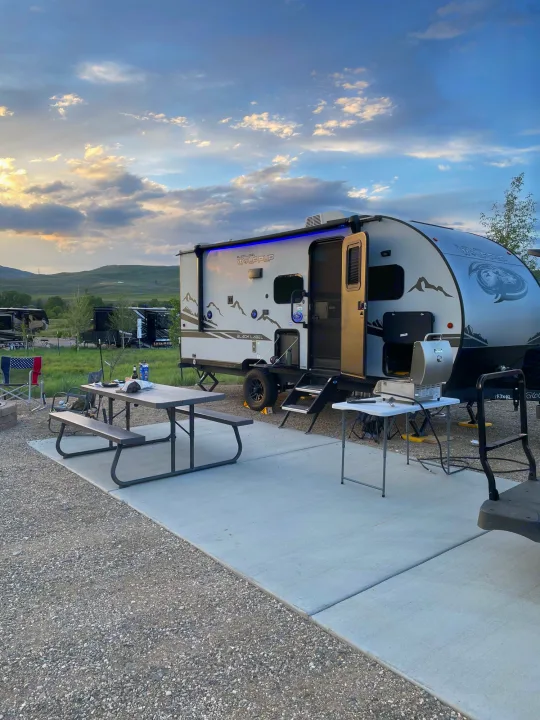 RV rental on a concrete pad at a campsite with a picnic table & grill, surrounded by nature and a sunset sky.. Forest River Cherokee Wolf Pup Black Label 2022