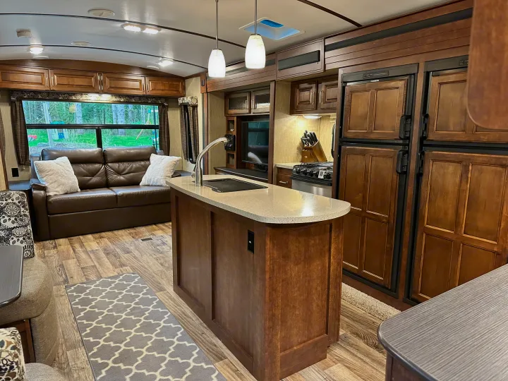 Step inside this inviting RV rental: a modern interior with a central kitchen island, wooden cabinetry, and a comfy sofa.. Keystone RV Outback Super-Lite 2018