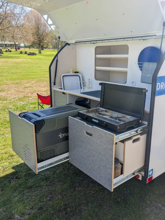This RV rental's rear outdoor kitchen setup: pull-out fridge, Primus stove, and sink for camping convenience.. DROPLET XL 2024
