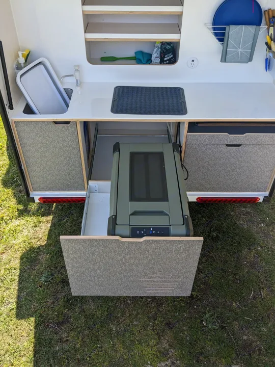 Compact RV rental galley with a pull-out fridge, sink, and organized storage for convenient outdoor cooking.. DROPLET XL 2024