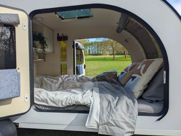 Step inside this cozy RV rental with a comfy bed, modern interior, and a scenic view of an open field. Ideal for camping.. DROPLET XL 2024