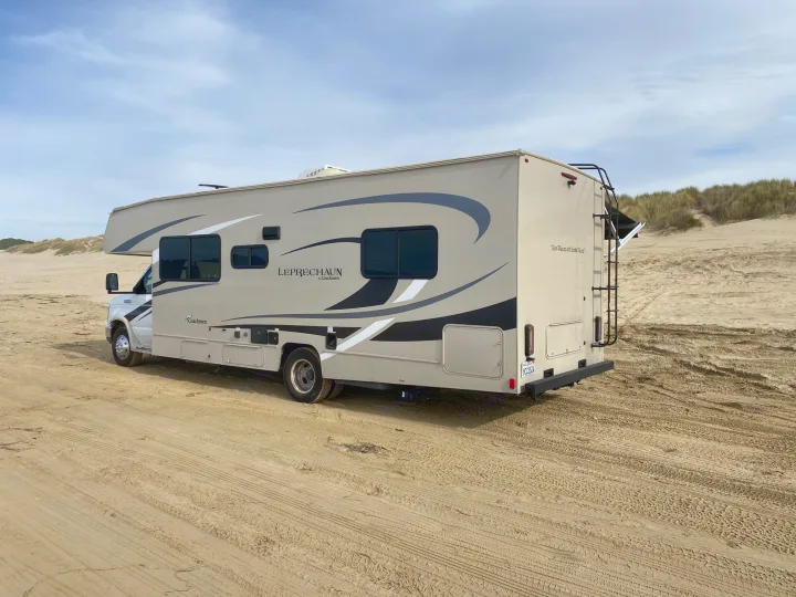 Explore coastal dunes with this Class C RV rental, a spacious home on sandy terrain under a cloudy sky.. Coachmen Leprechaun 2021