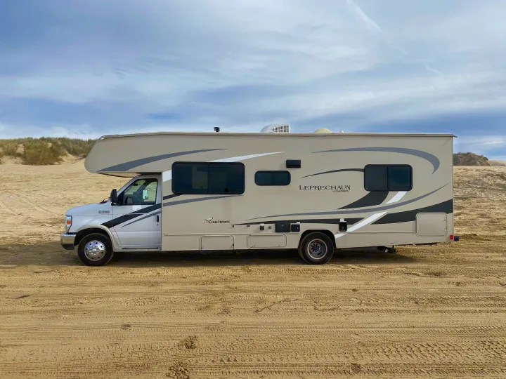 This Class C RV rental, a Coachmen Leprechaun, sits on sandy dunes under a cloudy sky, ideal for off-road travel.. Coachmen Leprechaun 2021