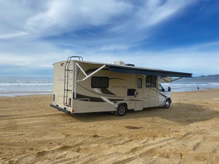 This RV rental is parked on a sandy beach with ocean waves in the background, offering freedom to explore.. Coachmen Leprechaun 2021