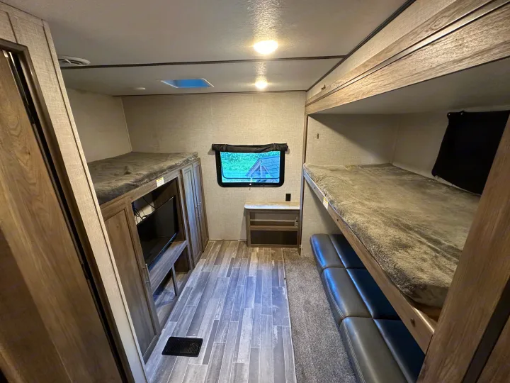 Cozy RV rental interior with bunk beds, TV, and a window view, offering comfortable sleeping and living space.. Crossroads RV Zinger 2021