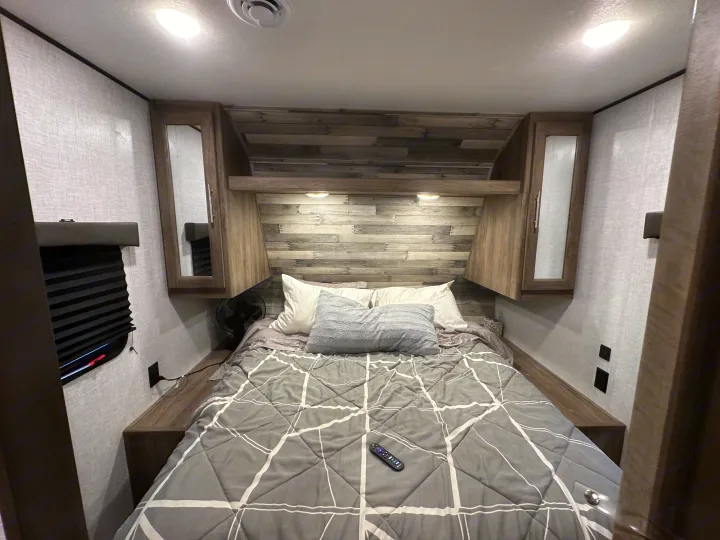 Cozy RV rental bedroom with a modern design, featuring a comfortable bed, wood accents, and overhead lighting.. Crossroads RV Zinger 2021