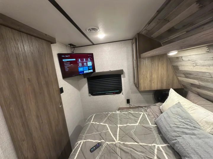 RV rental bedroom with a wall-mounted TV, comfortable bed, compact storage, and wood-like interior.. Crossroads RV Zinger 2021