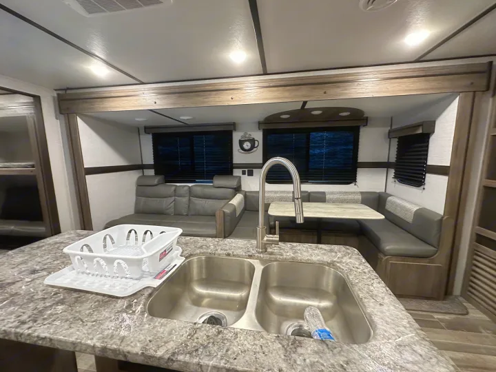 Spacious RV rental interior featuring a modern kitchen with double sink, cozy sofa, and dining booth.. Crossroads RV Zinger 2021