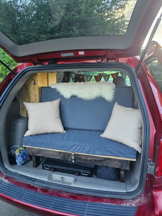 This custom minivan conversion features a cozy camper bed, ideal for an RV rental or road trip adventure. Interior view.. Dodge Caravan 2003