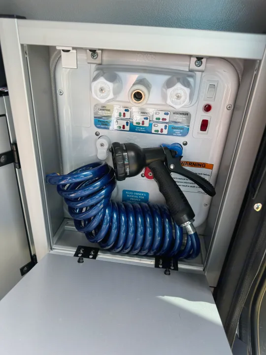 RV rental water utility hub: Nautilus panel, coiled hose, and nozzle for fresh water, city hookup, and winterizing.. Winnebago Revel 2023