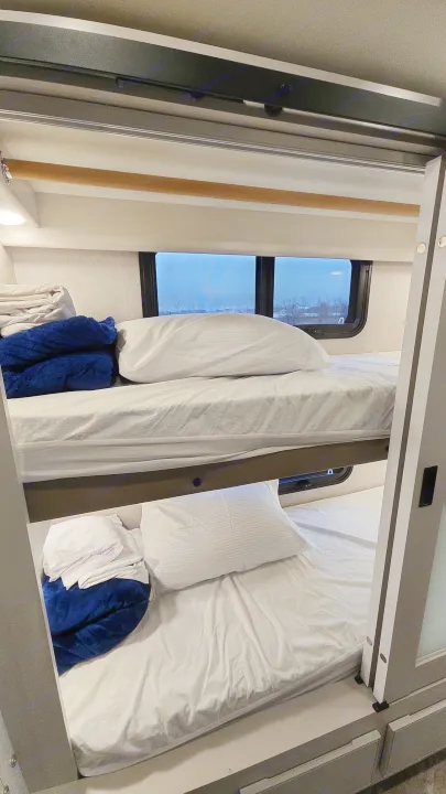 Comfortable bunk beds in an rv rental, featuring white sheets, blue blankets, and a window view.. Holiday Rambler Eclipse 2024