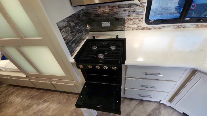 Modern rv rental kitchen featuring a black gas stove/oven, patterned backsplash, and light gray storage cabinets.. Holiday Rambler Eclipse 2024
