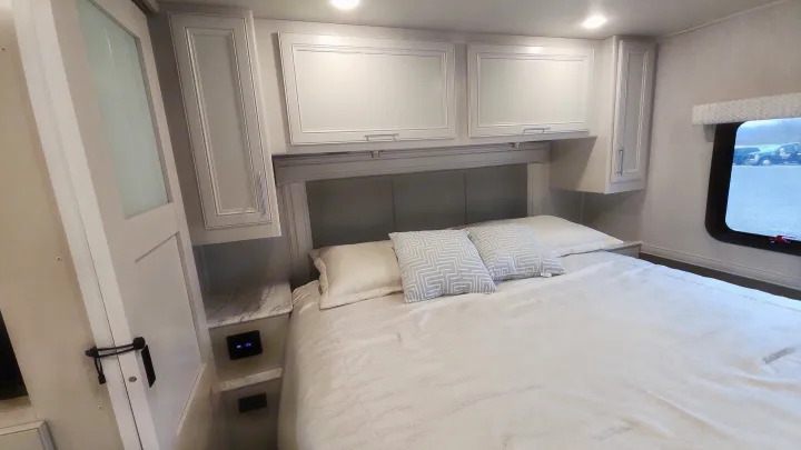 Relax in this modern RV rental bedroom featuring a queen bed, gray upholstered headboard, and convenient overhead storage.. Holiday Rambler Eclipse 2024