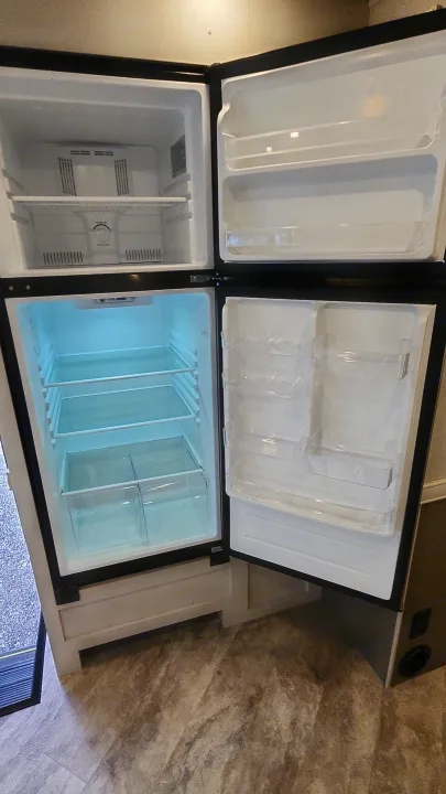 An empty, two-door RV rental refrigerator and freezer, showcasing its clean interior and spacious shelves.. Holiday Rambler Eclipse 2024