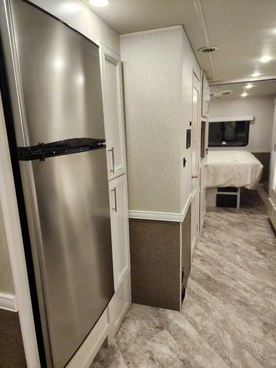 View inside a modern RV rental, featuring a stainless steel refrigerator, light cabinetry, and patterned walls, extending to a bedroom area.. Holiday Rambler Eclipse 2024