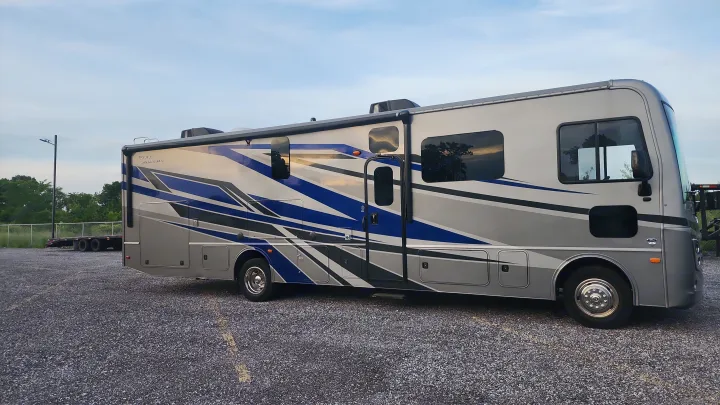 A large, silver and blue motorhome RV rental is parked on a gravel lot, waiting under a clear sky.. Holiday Rambler Eclipse 2024