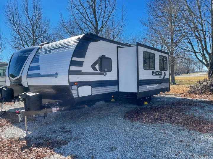 A Zinger Lite travel trailer, potentially an RV rental, with its slide-out extended on a gravel lot.. Crossroads RV Zinger Lite 2021