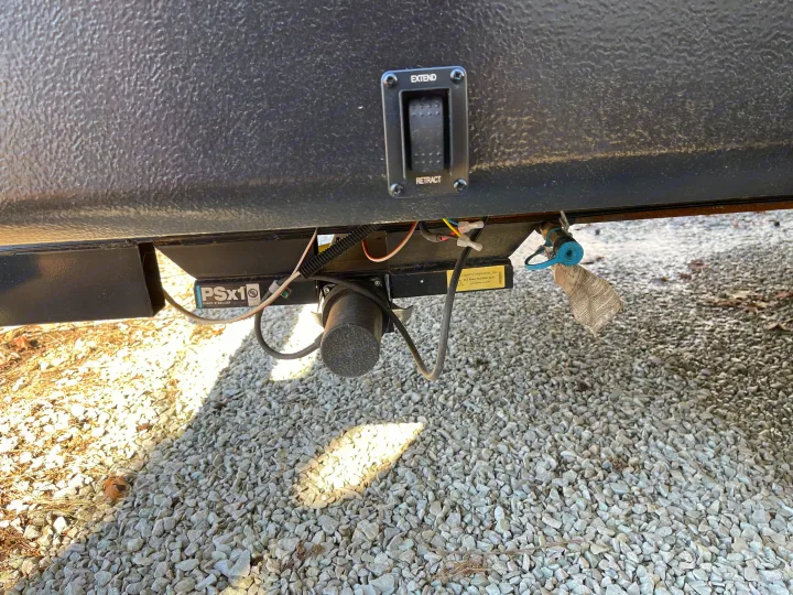 RV rental: A power stabilizer jack (Lippert PSx1) and its extend/retract control switch under an RV, on gravel.. Crossroads RV Zinger Lite 2021