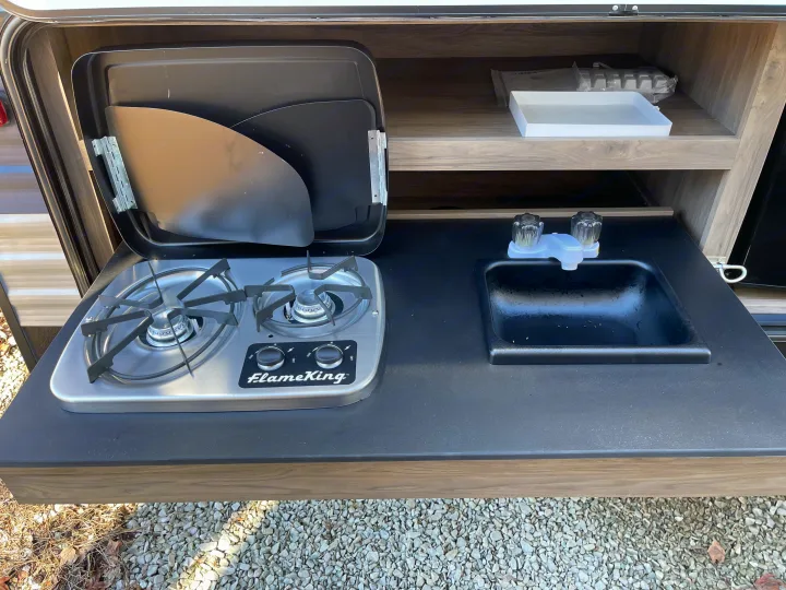 This RV rental's outdoor kitchen includes a two-burner stove, sink, and storage for convenient camping.. Crossroads RV Zinger Lite 2021