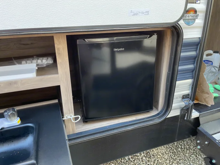 RV rental's outdoor kitchen, featuring a Hotpoint mini-fridge, sink, and storage compartment. Ideal for camping.. Crossroads RV Zinger Lite 2021