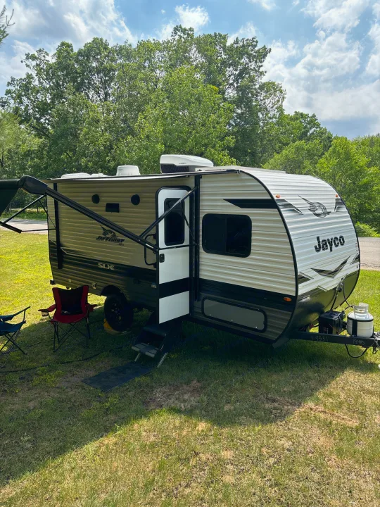 Jayco travel trailer RV rental at a sunny campground. Awning extended, chairs out, ready for outdoor adventure.. Jayco Jay Flight SLX 2024