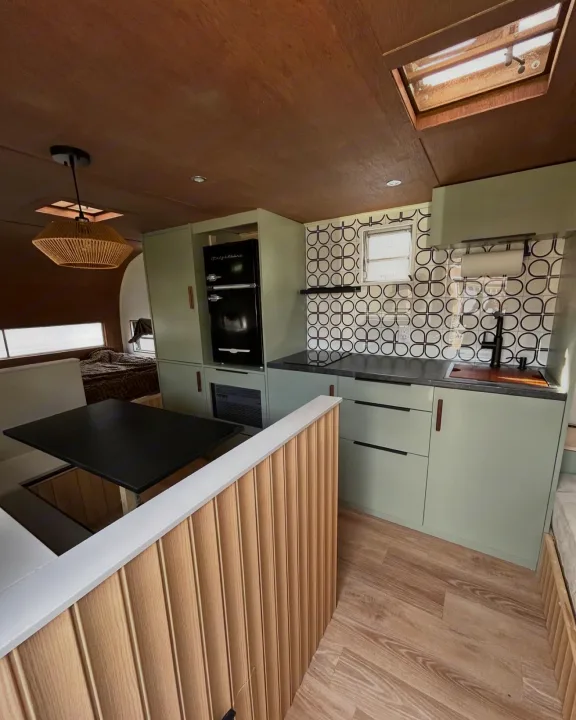 Modern RV rental interior featuring a sage green kitchen, cozy dining area, and bedroom. Wood ceilings and floors create a warm feel.. Glendale Golden Falcon 1967