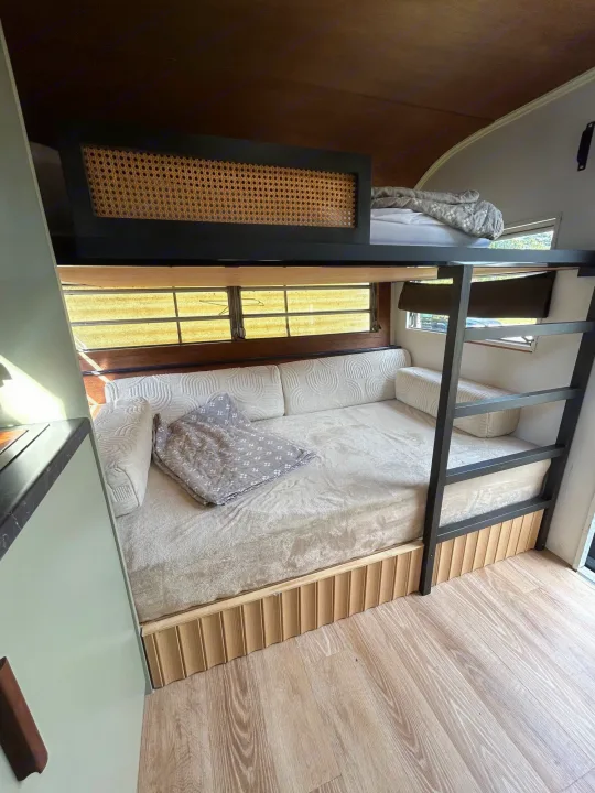 Cozy RV rental interior featuring a bunk bed setup with a lower sofa bed, upper rattan-paneled bunk, and wood accents. Perfect for mobile living.. Glendale Golden Falcon 1967