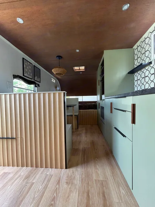 Modern RV rental interior: Light green kitchen, wood fluted divider, and wooden floors create a bright, functional space.. Glendale Golden Falcon 1967
