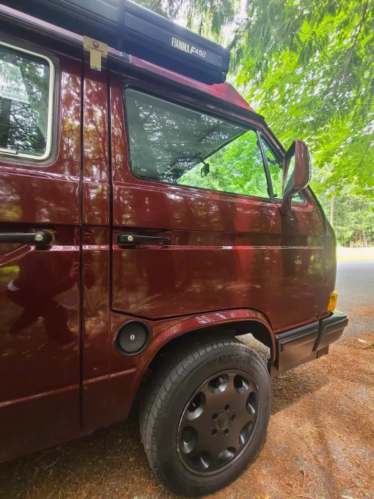 Side of a burgundy camper van with a Fiamma F45S awning, parked outdoors. Ideal for your next rv rental adventure.. Volkswagen T3 Mulitvan 1991