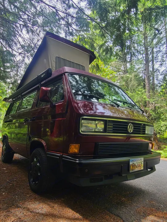Maroon VW Vanagon pop-top camper van with awning, parked in a forest in BC. Perfect rv rental for outdoor trips.. Volkswagen T3 Mulitvan 1991