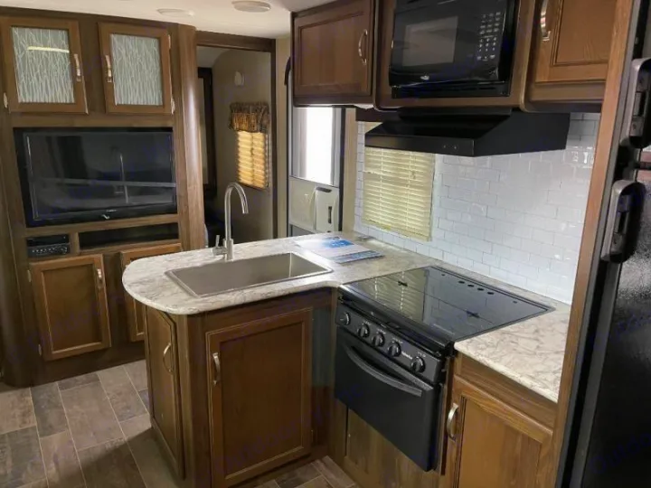 Well-equipped RV rental interior: kitchen with island, sink, stove, microwave, and TV setup for your travels.. Keystone RV Bullet Ultra Lite 2018