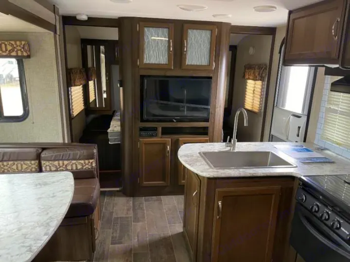 RV rental interior featuring a full kitchen with sink and stove, dining booth, TV, and a peek into a sleeping area.. Keystone RV Bullet Ultra Lite 2018