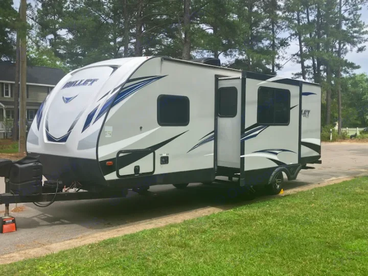 A sleek white Bullet travel trailer, an excellent RV rental option, parked outside with its door open.. Keystone RV Bullet Ultra Lite 2018