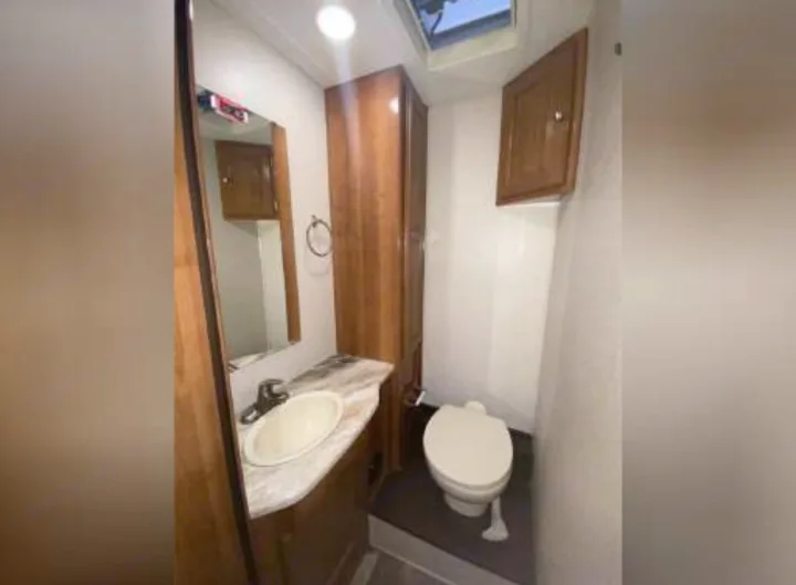 Inside an RV rental: a compact bathroom featuring a vanity with sink, mirror, toilet on a raised platform, and storage cabinets.. Coachmen Leprechaun 270QB 2019