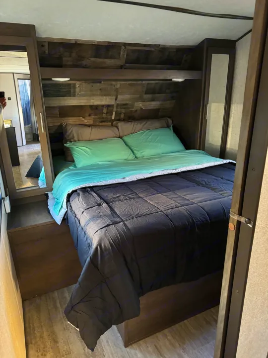 Cozy RV rental bedroom with rustic wood accent wall and built-in storage. Ideal for comfort on the road.. Aspen Trail Aspen Trail Trailer 2021