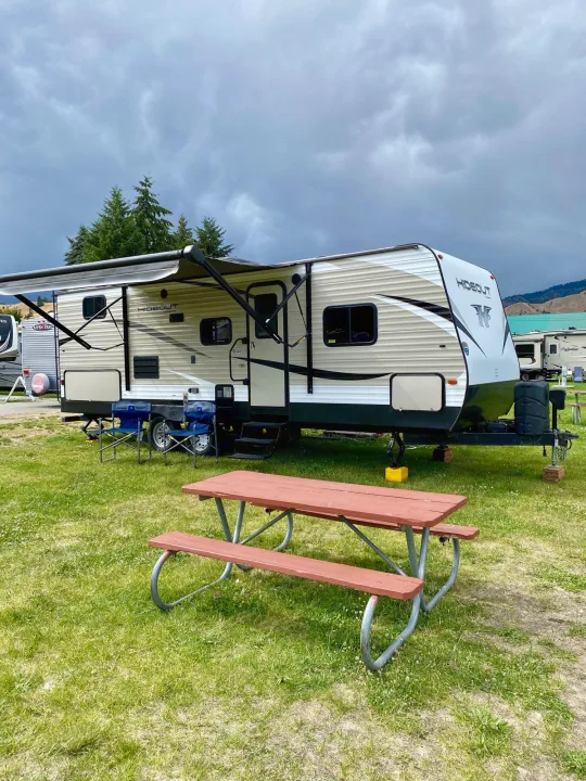 Spacious Hideout **RV rental** at a scenic campground with an extended awning, chairs, and a picnic table under a cloudy sky.. Keystone RV Hideout 2018
