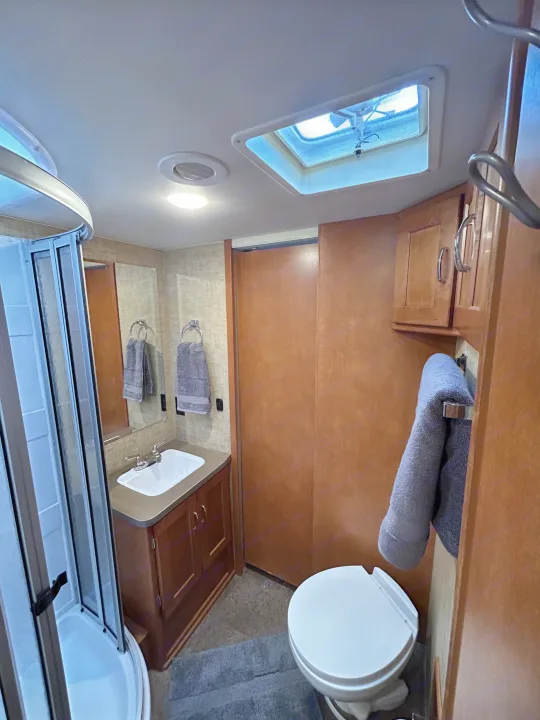 Inside an rv rental: a well-equipped RV bathroom featuring a shower, toilet, sink, and overhead skylight.. Winnebago Minnie Winnie 2017