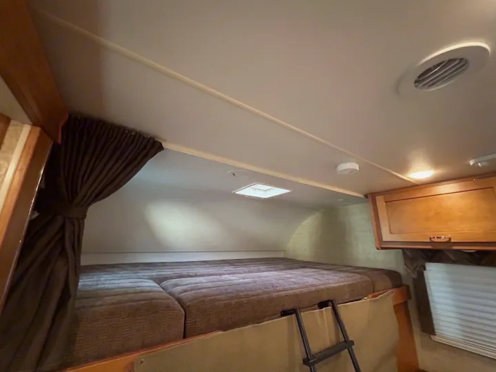 An RV rental's cozy interior features a large overhead bed, access ladder, curtains, and cabinets, ready for your adventure.. Winnebago Minnie Winnie 2017